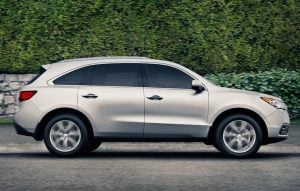 2015 Acura MDX side view driving on the street against a wall of bushes