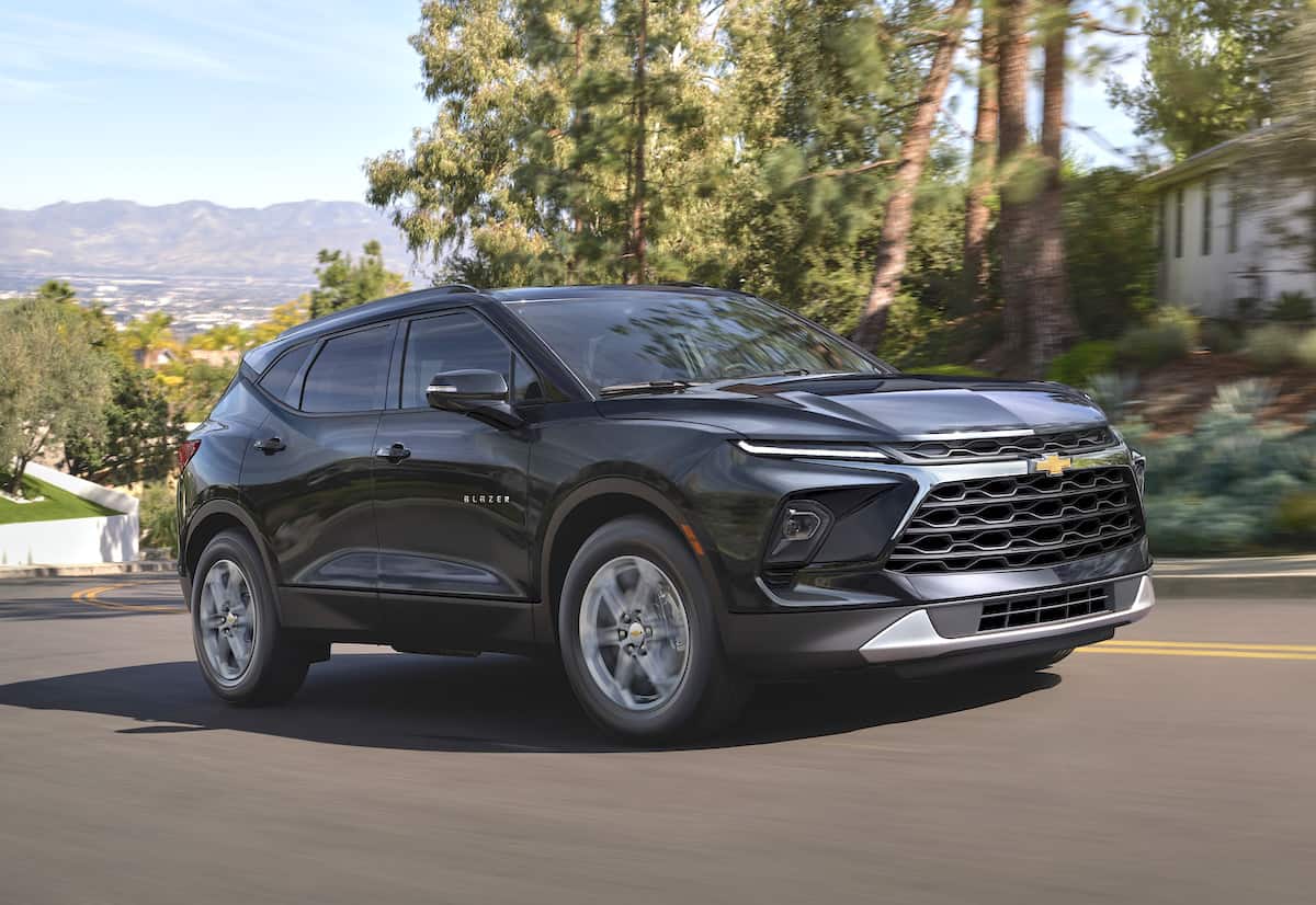 Front 3/4 view of the 2024 Chevrolet Blazer 3LT in Black, driving in front of a home.